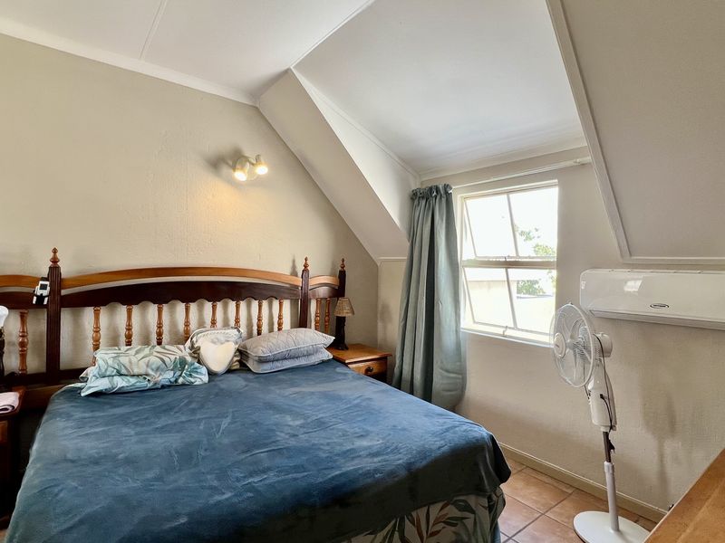 A cozy bedroom featuring a sloped ceiling, tiled flooring, and a wall-mounted air conditioning unit.