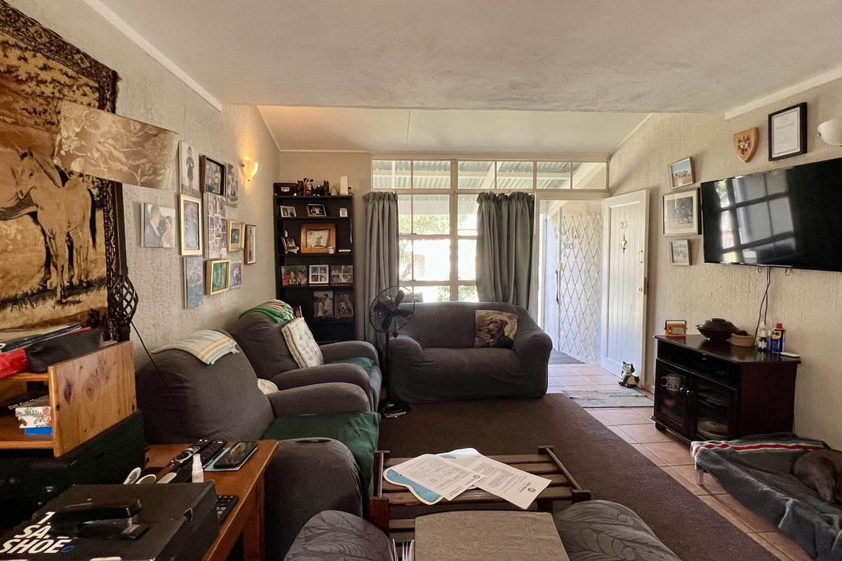 A comfortable living room featuring tiled flooring, large windows allowing natural light, and direct access to the exterior through a security gate.