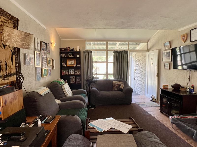 A comfortable living room featuring tiled flooring, large windows allowing natural light, and direct access to the exterior through a security gate.