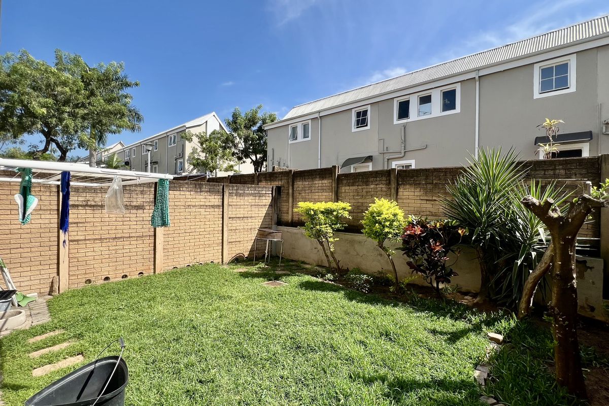 A private rear garden featuring a lawn area, established shrubs, and a high brick boundary wall, providing a secure outdoor space.