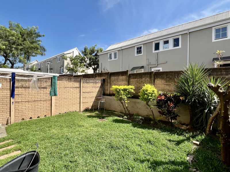 A private rear garden featuring a lawn area, established shrubs, and a high brick boundary wall, providing a secure outdoor space.