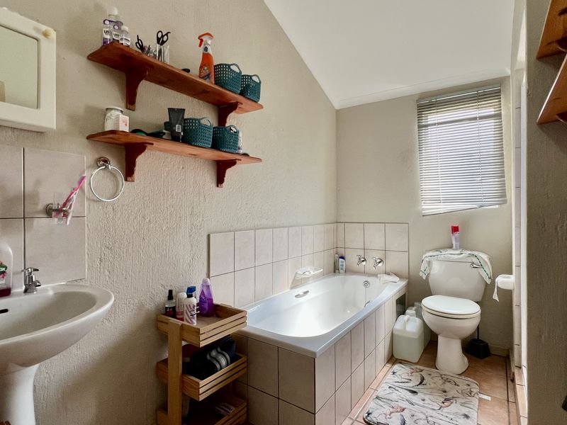A functional bathroom featuring a built-in bathtub, pedestal basin, and toilet, with tiled splashbacks and a window providing natural light.