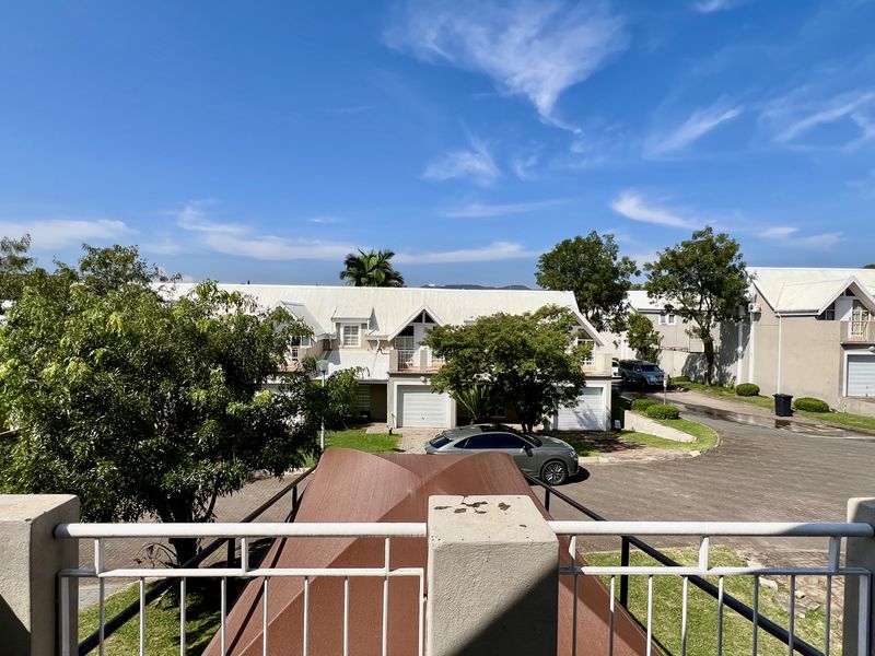 Elevated view overlooking a residential complex with paved driveways, garages, and landscaped garden areas under a clear blue sky.