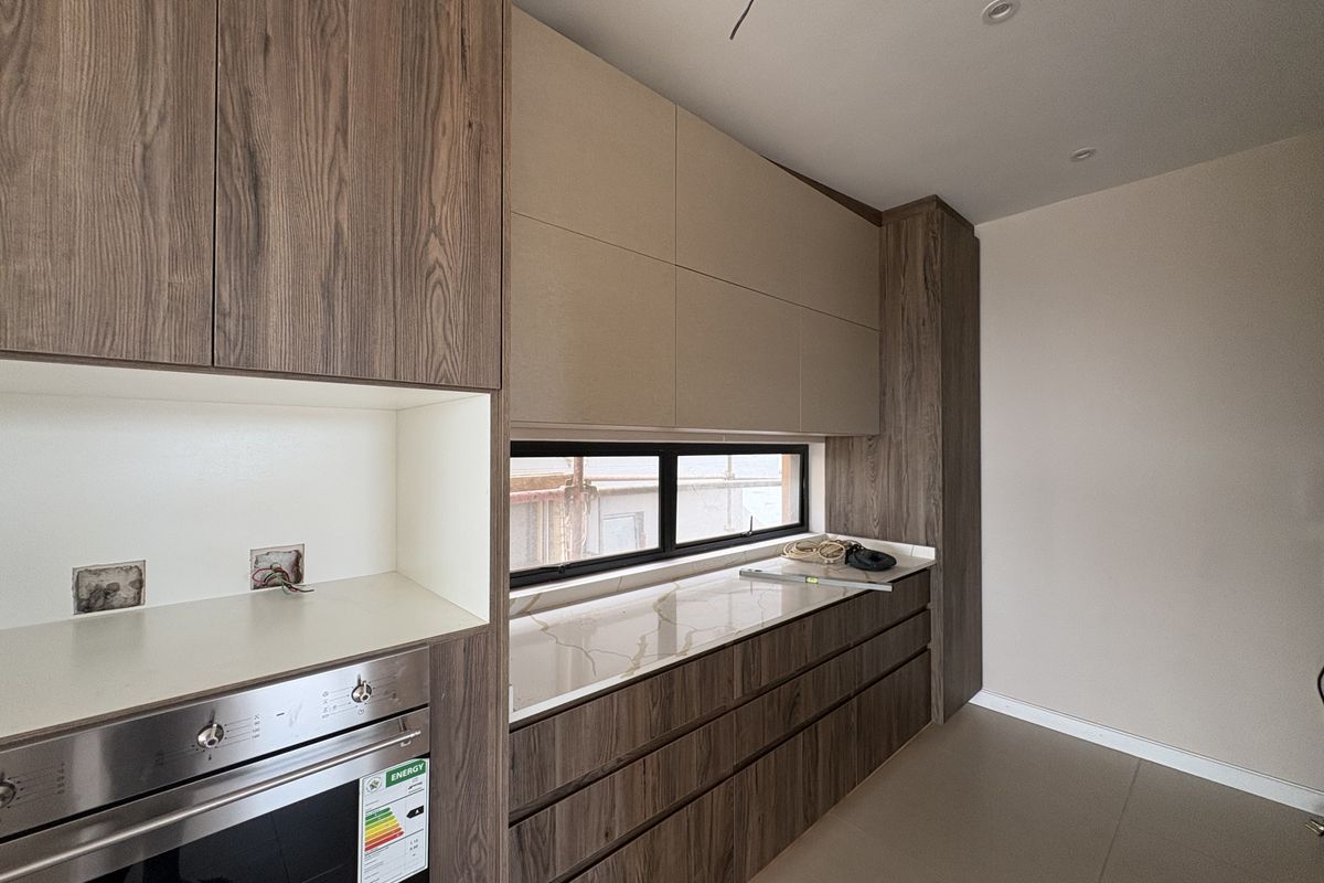 Modern kitchen featuring wood-grain cabinetry, stone countertops, and a built-in oven, currently undergoing final finishing touches.