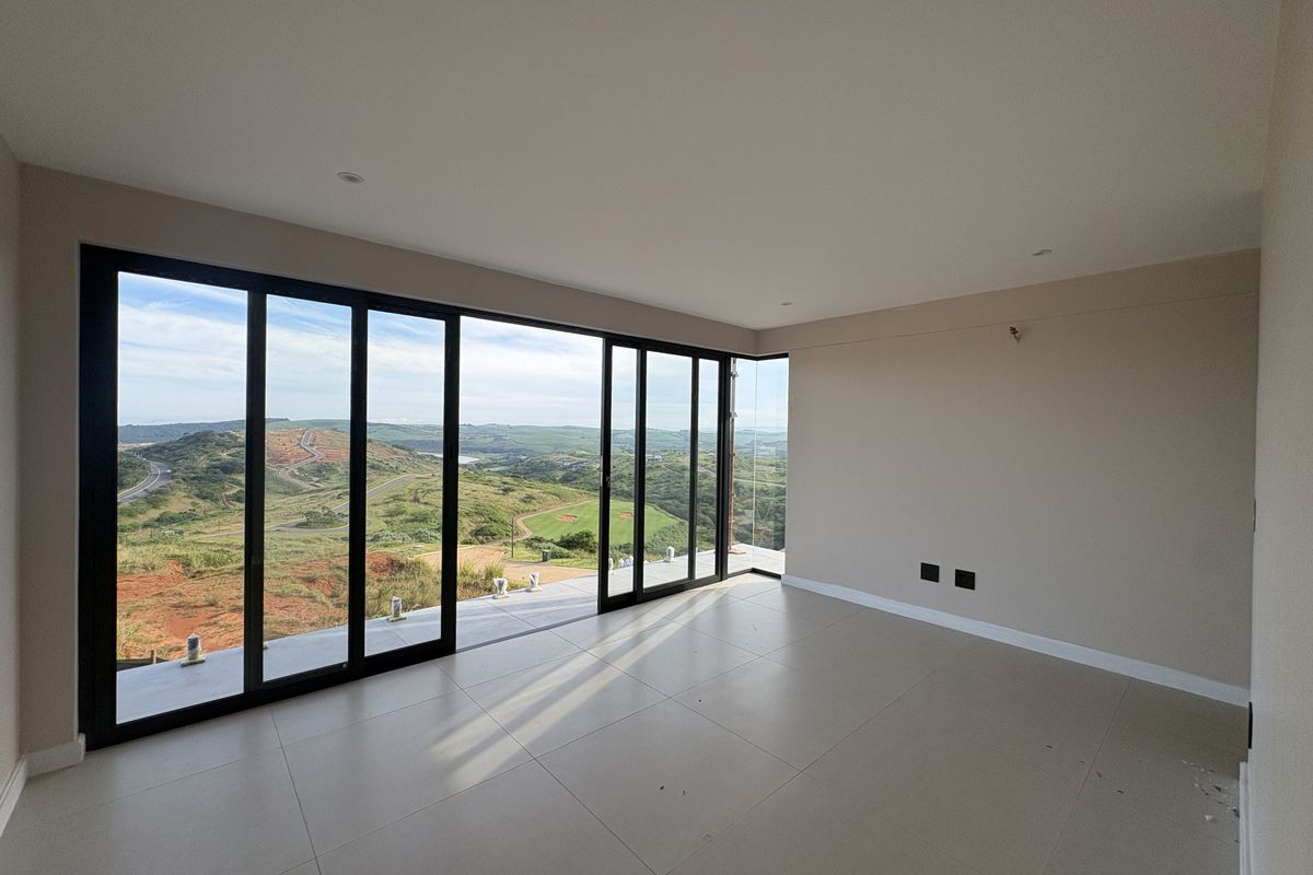 A bright, empty living room featuring large floor-to-ceiling sliding glass doors that open onto a balcony with expansive panoramic landscape views.