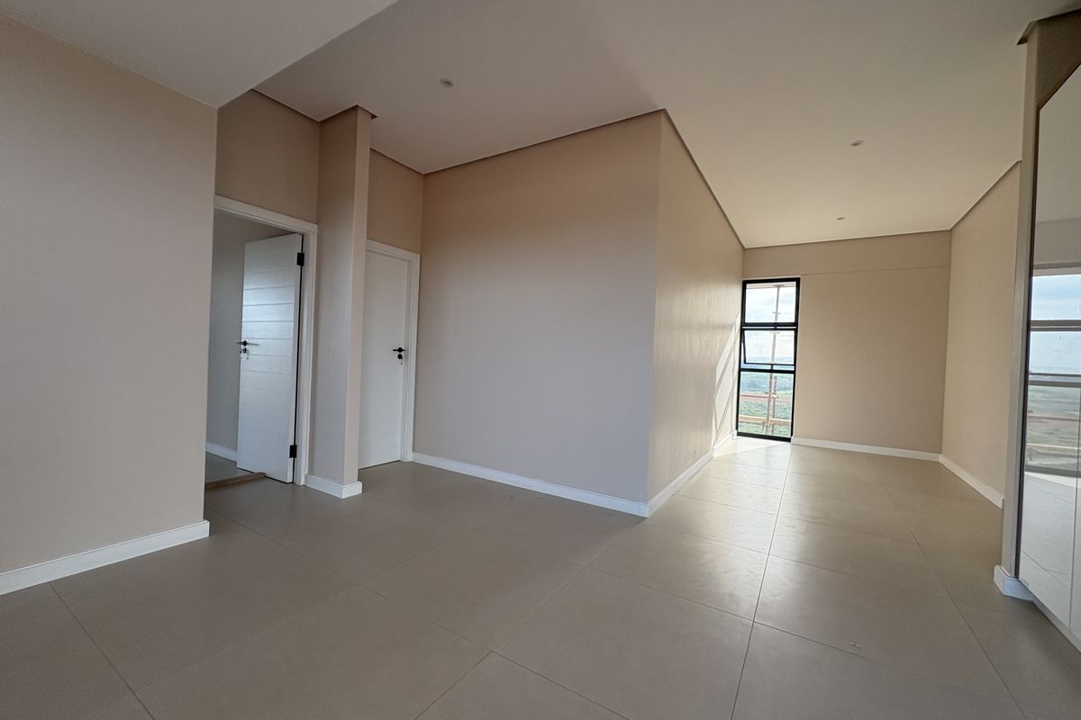 A bright, spacious, and modern bedroom featuring neutral wall tones, large format floor tiles, and a built-in wardrobe with mirrored doors.
