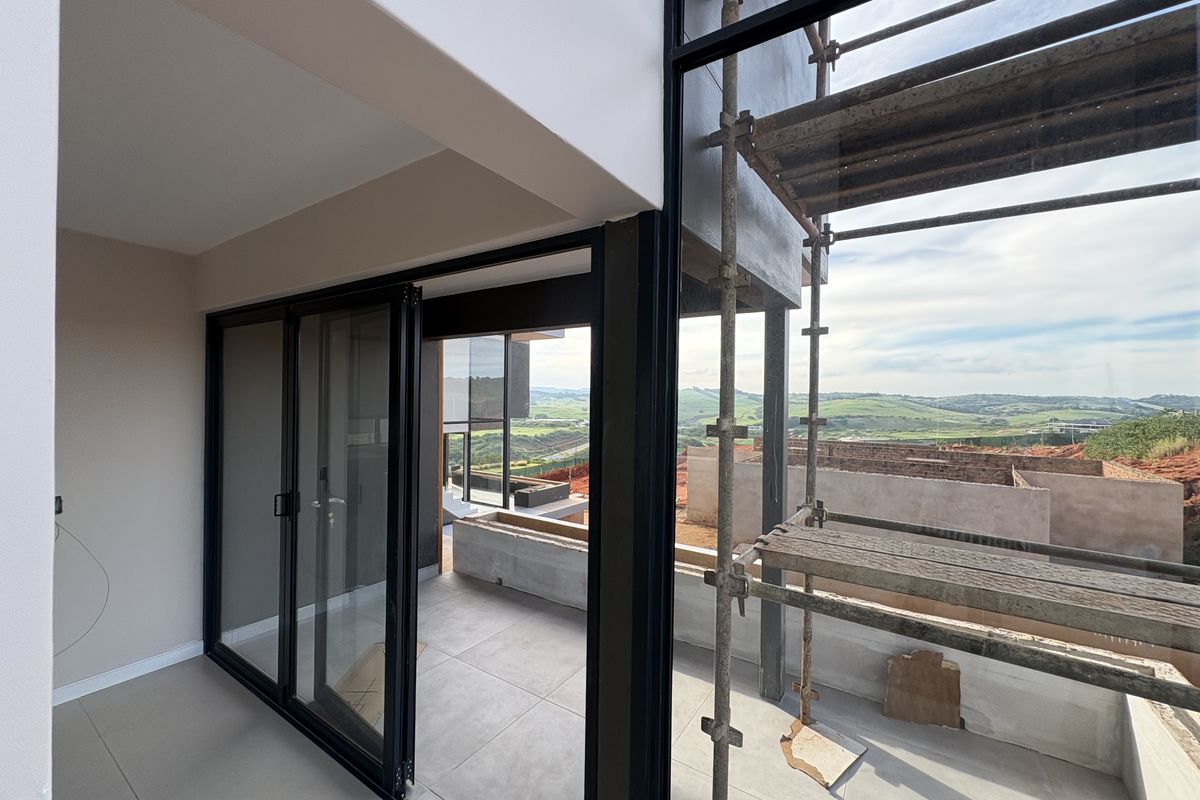 Modern interior space featuring large black-framed sliding glass doors leading to an outdoor balcony with scenic landscape views, currently under construction.