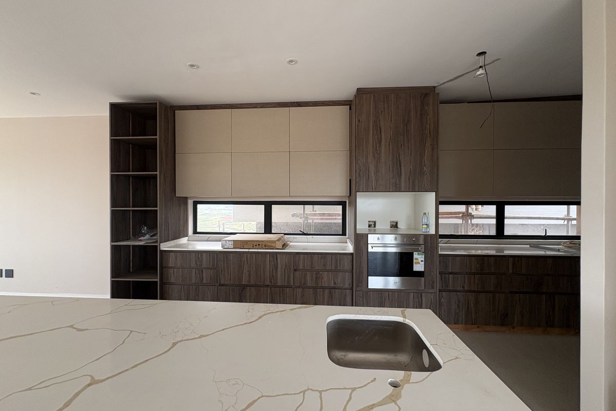 Modern kitchen featuring dark wood cabinetry, stone countertops with marble-effect veining, a central island with an integrated sink, and a built-in oven.
