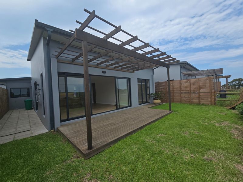 Rear view of the townhouse featuring a timber deck with a pergola, sliding glass doors, and a private garden area.