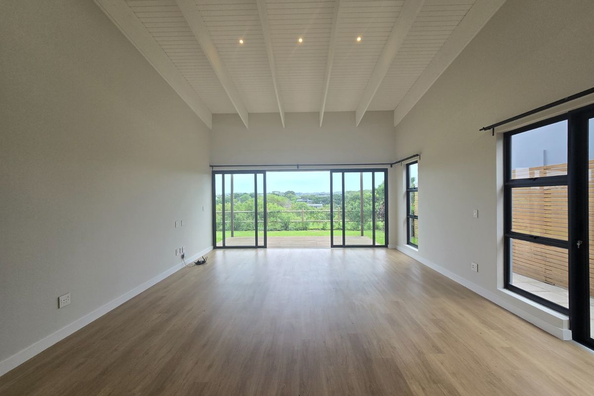 Spacious, light-filled living area featuring vaulted ceilings with exposed beams, modern laminate flooring, and large sliding doors opening to an outdoor deck.