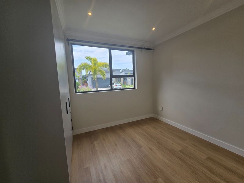 A bright, empty bedroom featuring modern laminate flooring, built-in cupboards, and recessed downlighting, offering a clean and neutral space ready for personalization.