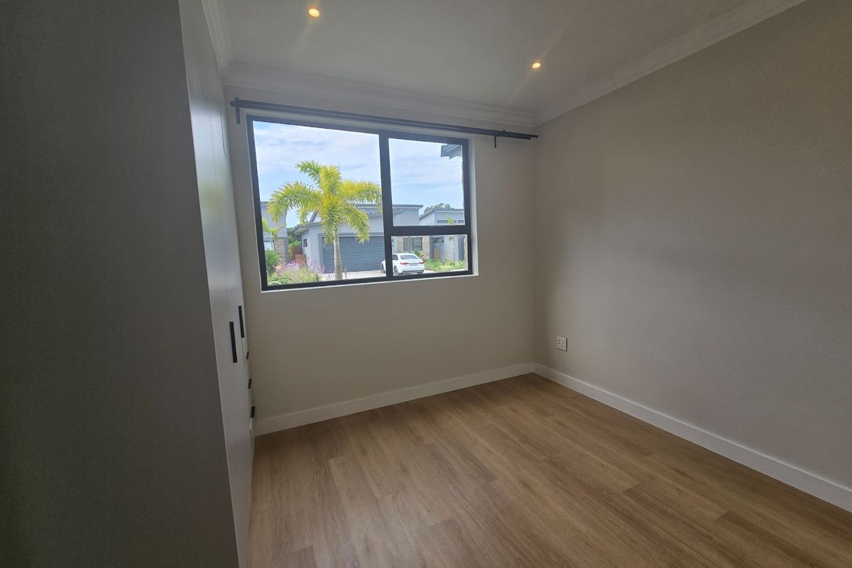 A bright, empty bedroom featuring modern laminate flooring, built-in cupboards, and recessed downlighting, offering a clean and neutral space ready for personalization.