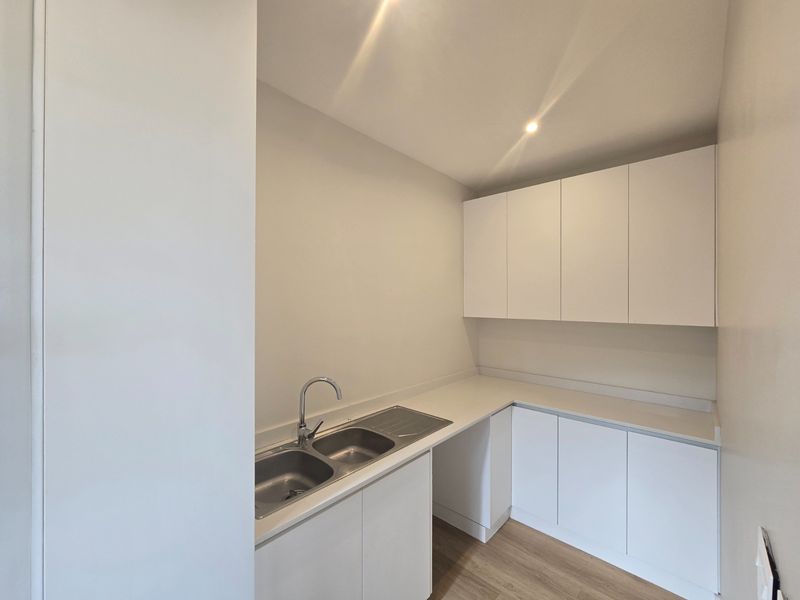A clean, modern scullery featuring white built-in cabinetry, a stainless steel double sink with mixer tap, and ample laminate countertop workspace.