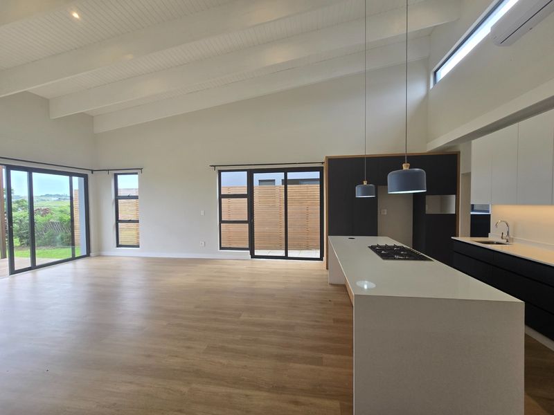 Spacious open-plan living and kitchen area featuring vaulted ceilings, modern cabinetry, a central island with gas cooktop, and large sliding doors to the exterior.