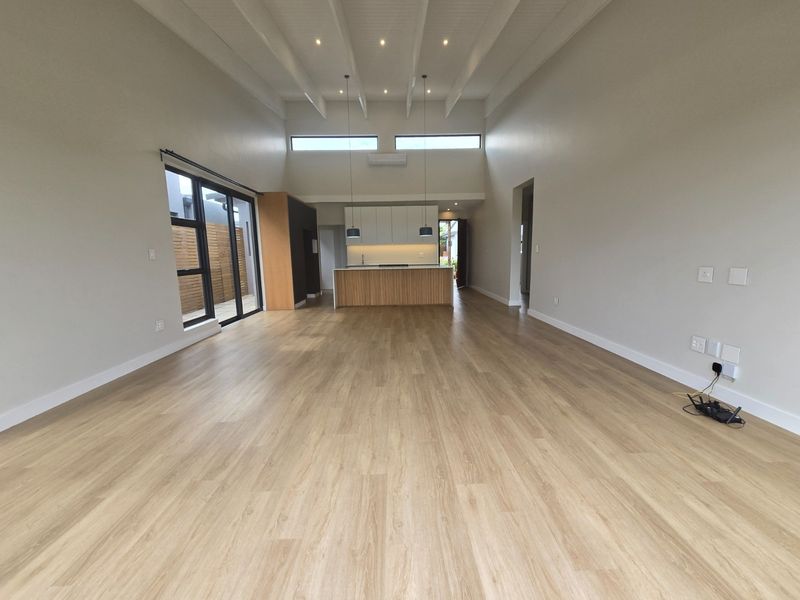 Spacious open-plan living and kitchen area featuring high vaulted ceilings, modern cabinetry, a central island, and light wood-look flooring throughout.