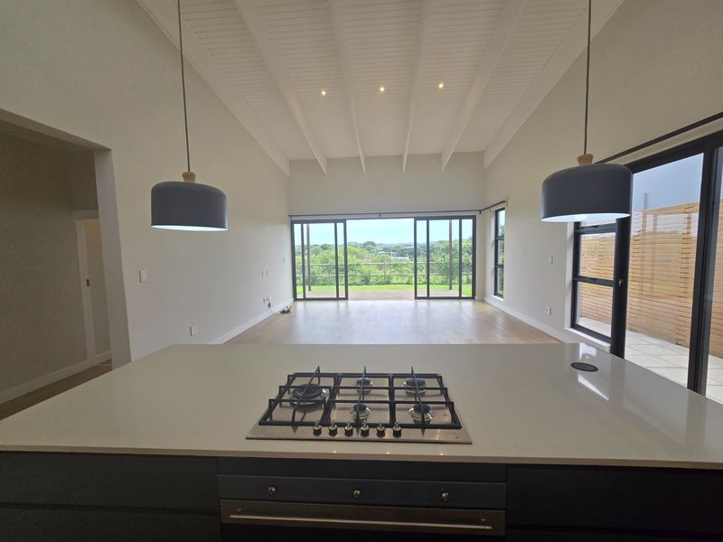 Spacious open-plan living area featuring a modern kitchen island with gas hob, vaulted ceilings with exposed beams, and large sliding doors opening to a deck.