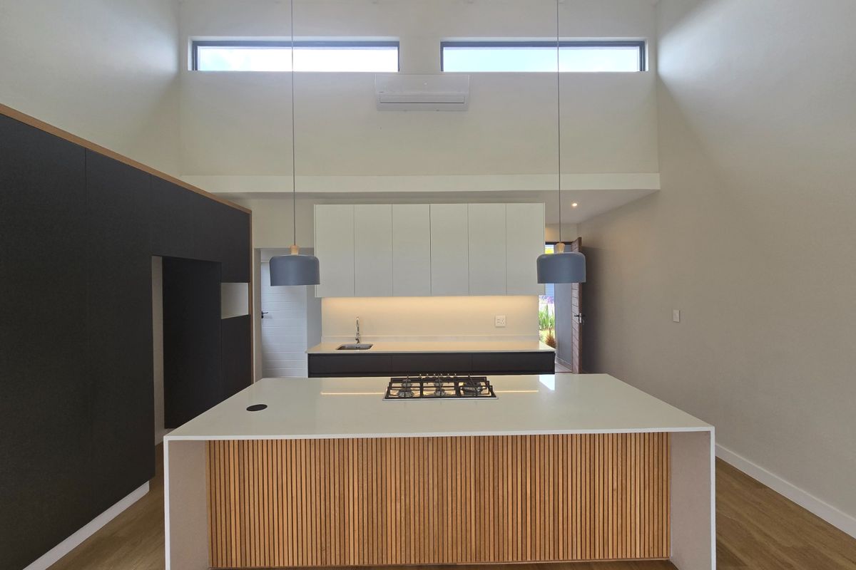 Modern kitchen featuring a central island with gas hob, sleek cabinetry, vaulted ceilings with clerestory windows, and high-quality finishes in an open-plan layout.