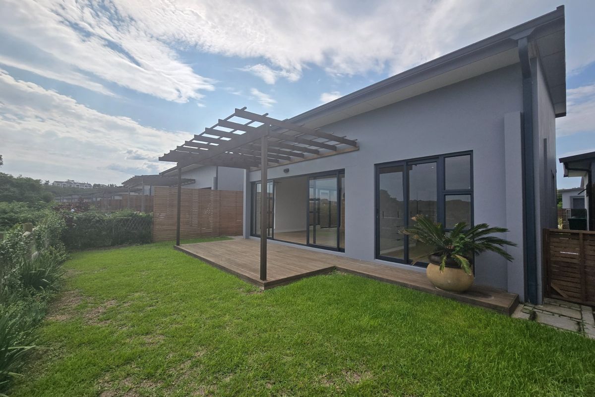 Rear view of the townhouse featuring a timber deck with a pergola, sliding glass doors, and a well-maintained garden area.
