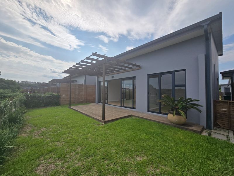 Rear view of the townhouse featuring a timber deck with a pergola, sliding glass doors, and a well-maintained garden area.