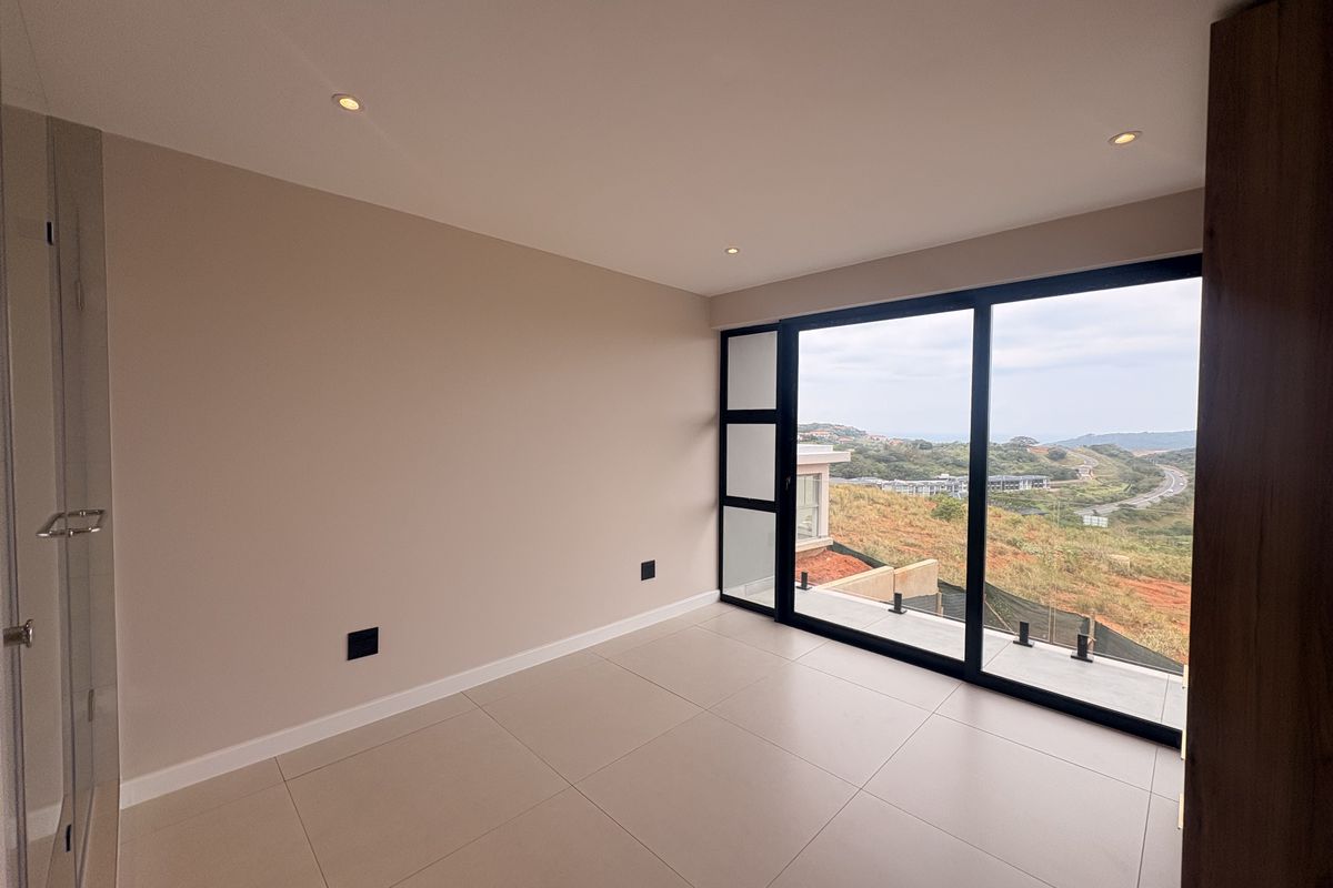 A bright, modern bedroom featuring large sliding glass doors that open to a balcony with scenic landscape views and tiled flooring.