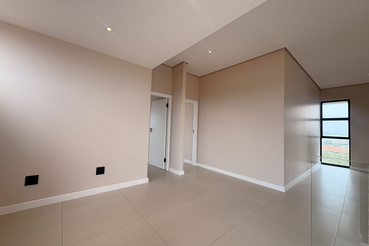 A bright, modern, and empty interior space featuring neutral-toned walls, large format floor tiles, recessed ceiling lighting, and a glass balustrade.