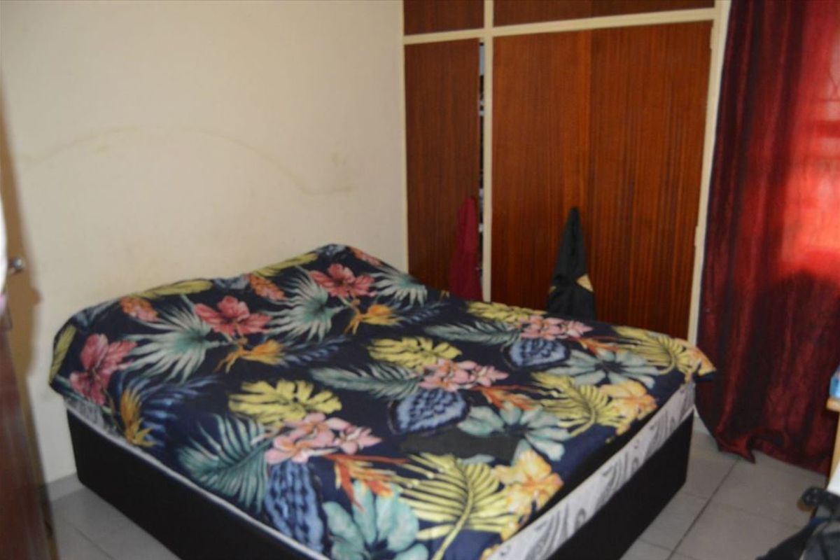 A bedroom featuring built-in wooden wardrobes and tiled flooring, offering a functional space with potential for cosmetic updates.