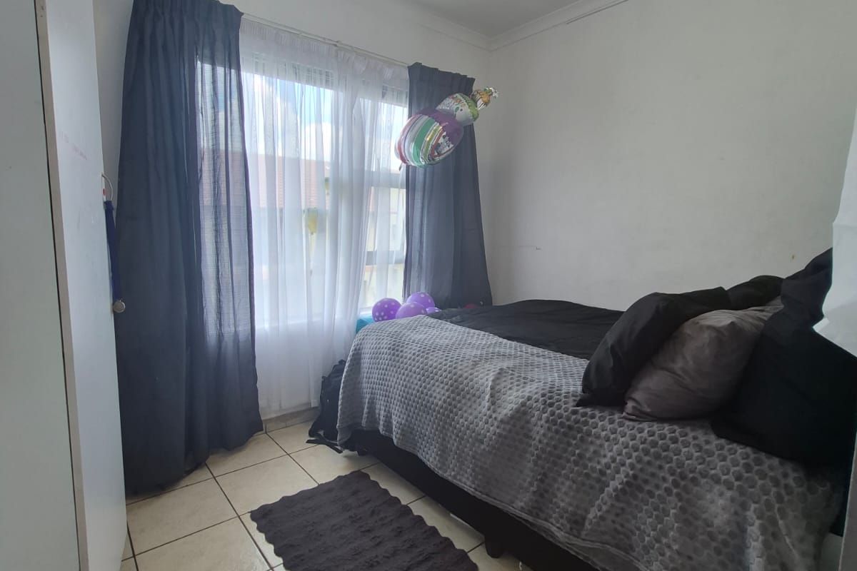 A compact bedroom featuring tiled flooring, a built-in wardrobe, and a window with curtain treatments.