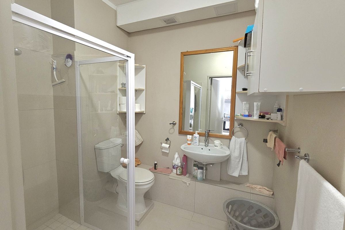 A functional bathroom featuring a glass-enclosed shower, pedestal sink, wall-mounted storage cabinetry, and neutral floor-to-ceiling tiling.