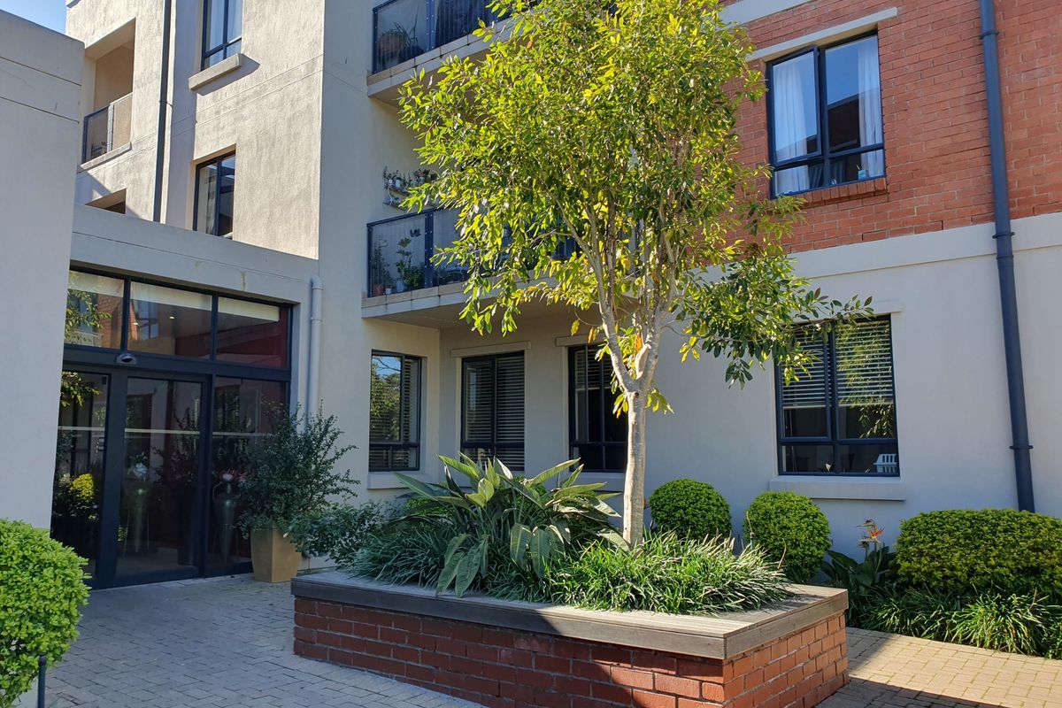 A well-maintained exterior courtyard area featuring a brick planter box, paved ground, and access to the apartment building entrance and balconies.