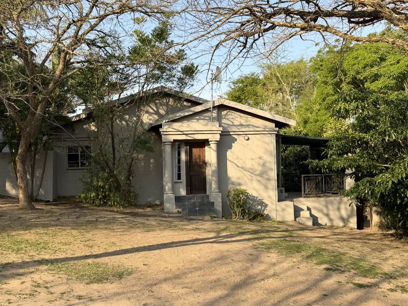 Front view of a single-story house featuring a covered entrance with columns, tiled steps, and mature surrounding trees.