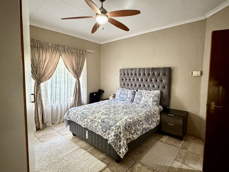 A comfortable bedroom featuring tiled flooring, a ceiling fan, and neutral wall tones, providing a functional and well-lit sleeping space.