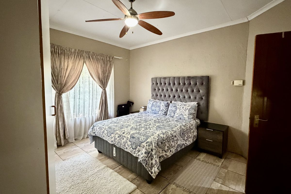 A comfortable bedroom featuring tiled flooring, a ceiling fan, and neutral wall tones, providing a functional and well-lit sleeping space.