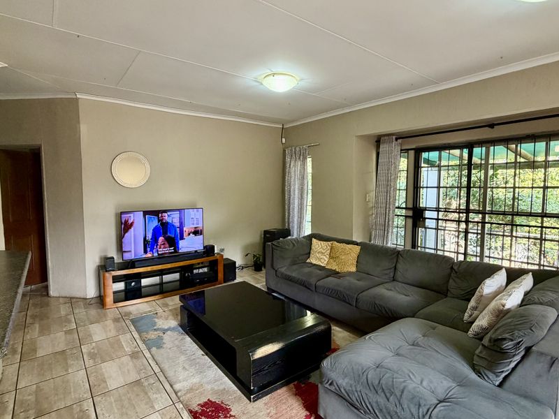 A comfortable living room featuring tiled flooring, a sliding glass door with security gate, and neutral wall tones, providing a functional and well-lit space.