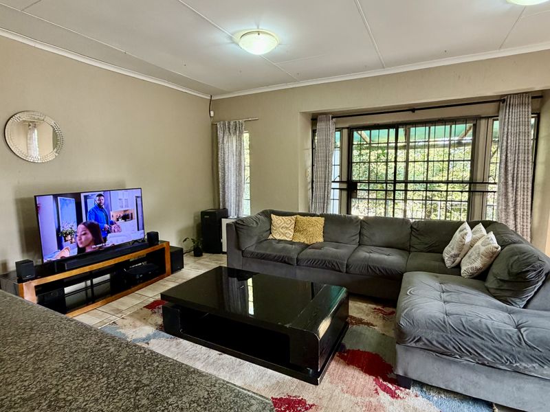 A comfortable living room featuring tiled flooring, coved ceilings, and large windows with security gates, providing a functional and well-lit space.