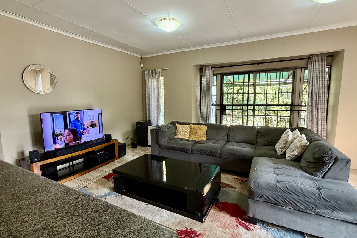 A comfortable living room featuring tiled flooring, coved ceilings, and large windows with security gates, providing a functional and well-lit space.