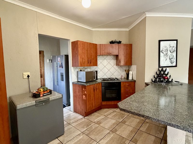 A functional kitchen featuring wood-tone cabinetry, granite-look laminate countertops, a built-in oven and hob, and a breakfast bar area with tiled flooring.