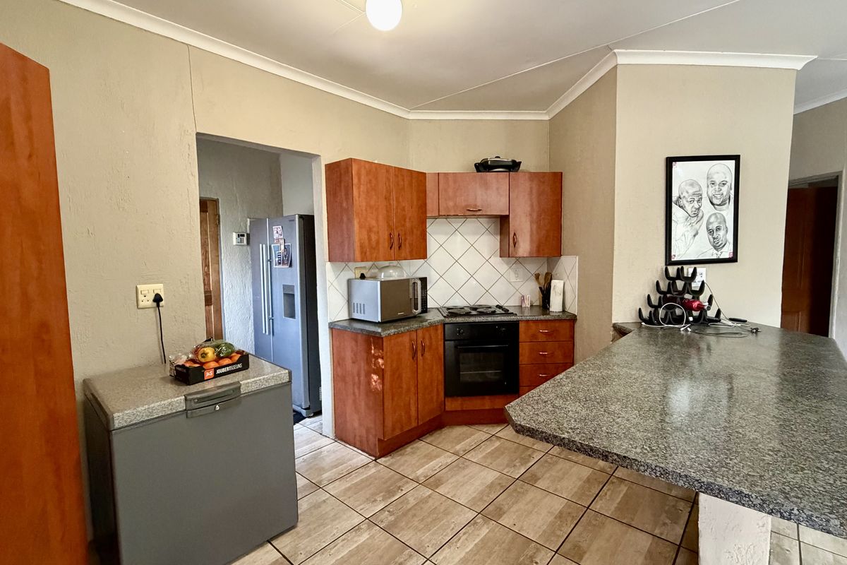 A functional kitchen featuring wood-tone cabinetry, granite-look laminate countertops, a built-in oven and hob, and a breakfast bar area with tiled flooring.