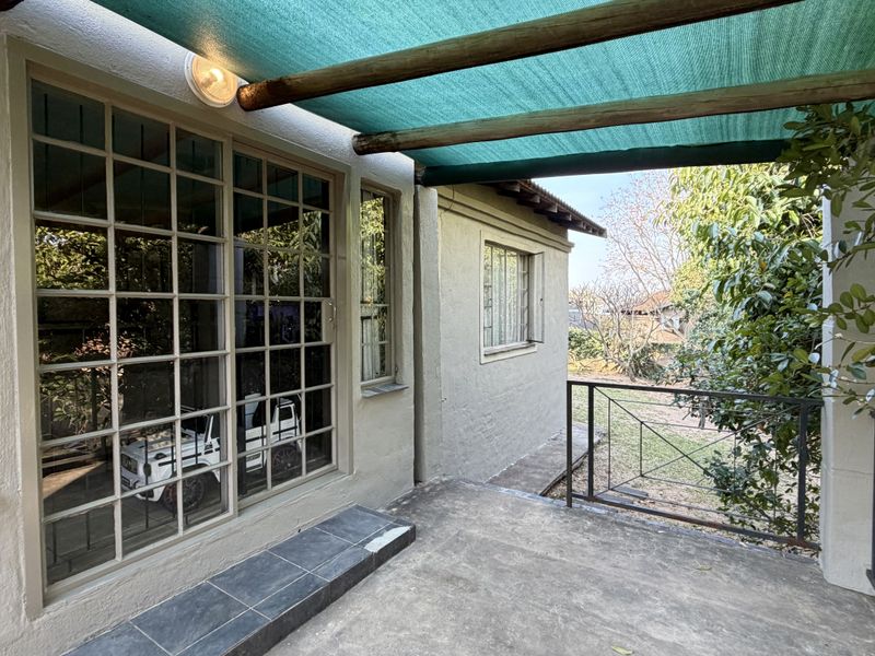 A covered patio area featuring a shade cloth pergola, concrete flooring, and metal railings, providing direct access to the garden through sliding glass doors.