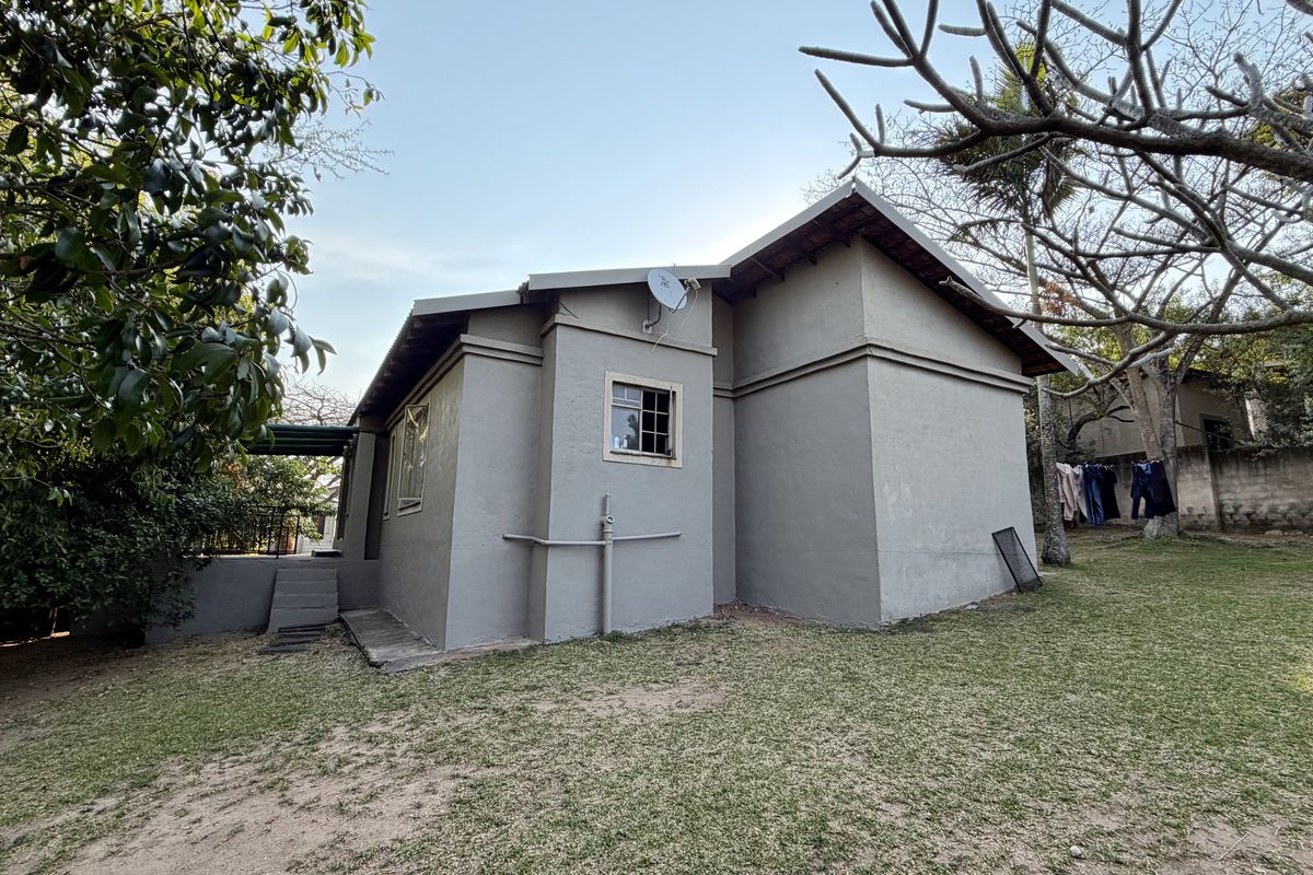 Rear view of the property showing the exterior wall, casement windows, and surrounding garden area with established trees.