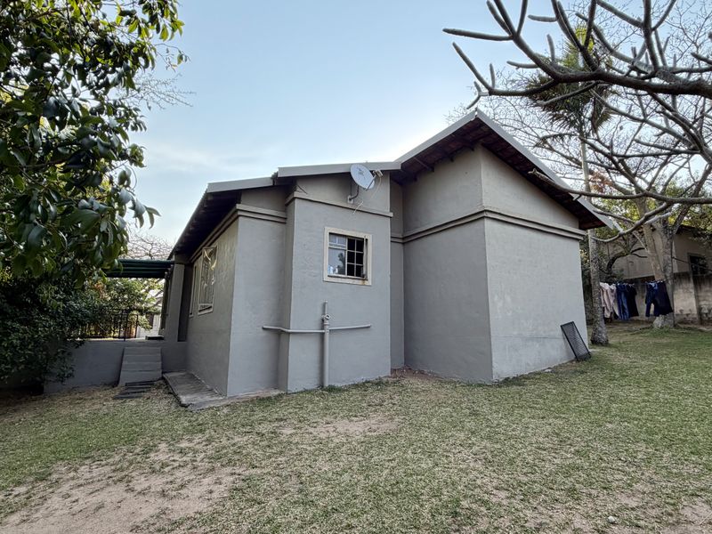 Rear view of the property showing the exterior wall, casement windows, and surrounding garden area with established trees.