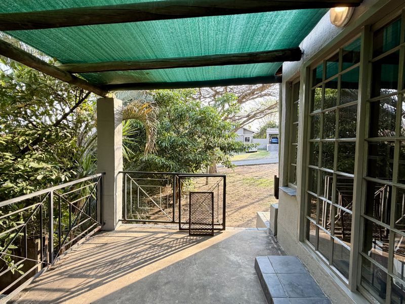 A covered outdoor patio area featuring a shade cloth canopy, metal balustrades, and large glass sliding doors leading into the home.
