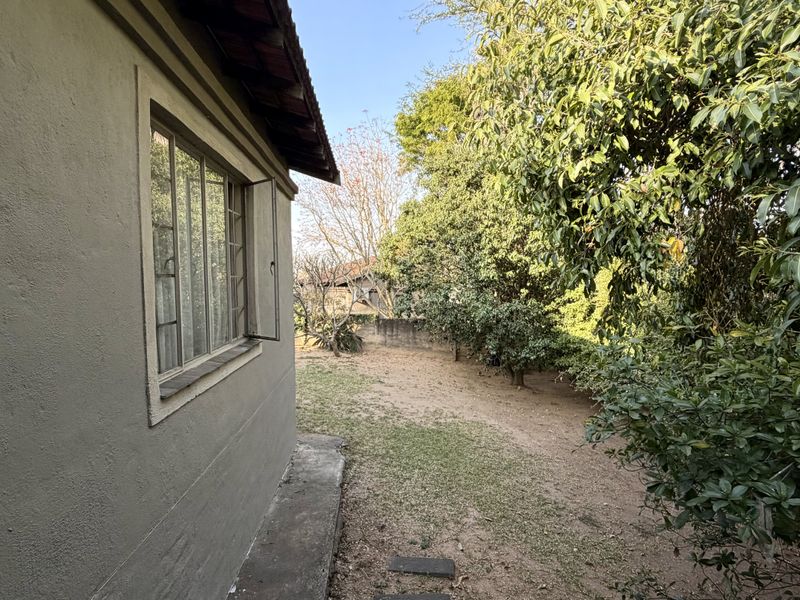 A view of the rear exterior of the property, featuring a concrete pathway alongside the building and a garden area with mature trees.