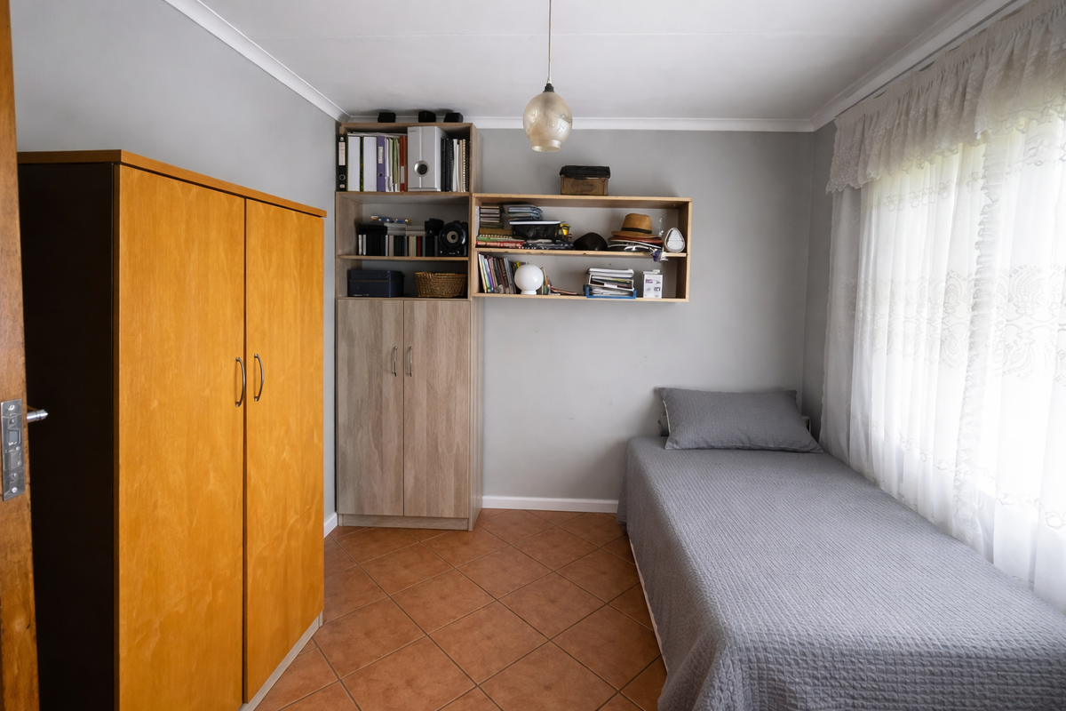 A functional bedroom featuring tiled flooring, built-in shelving, and a window with curtain treatments.
