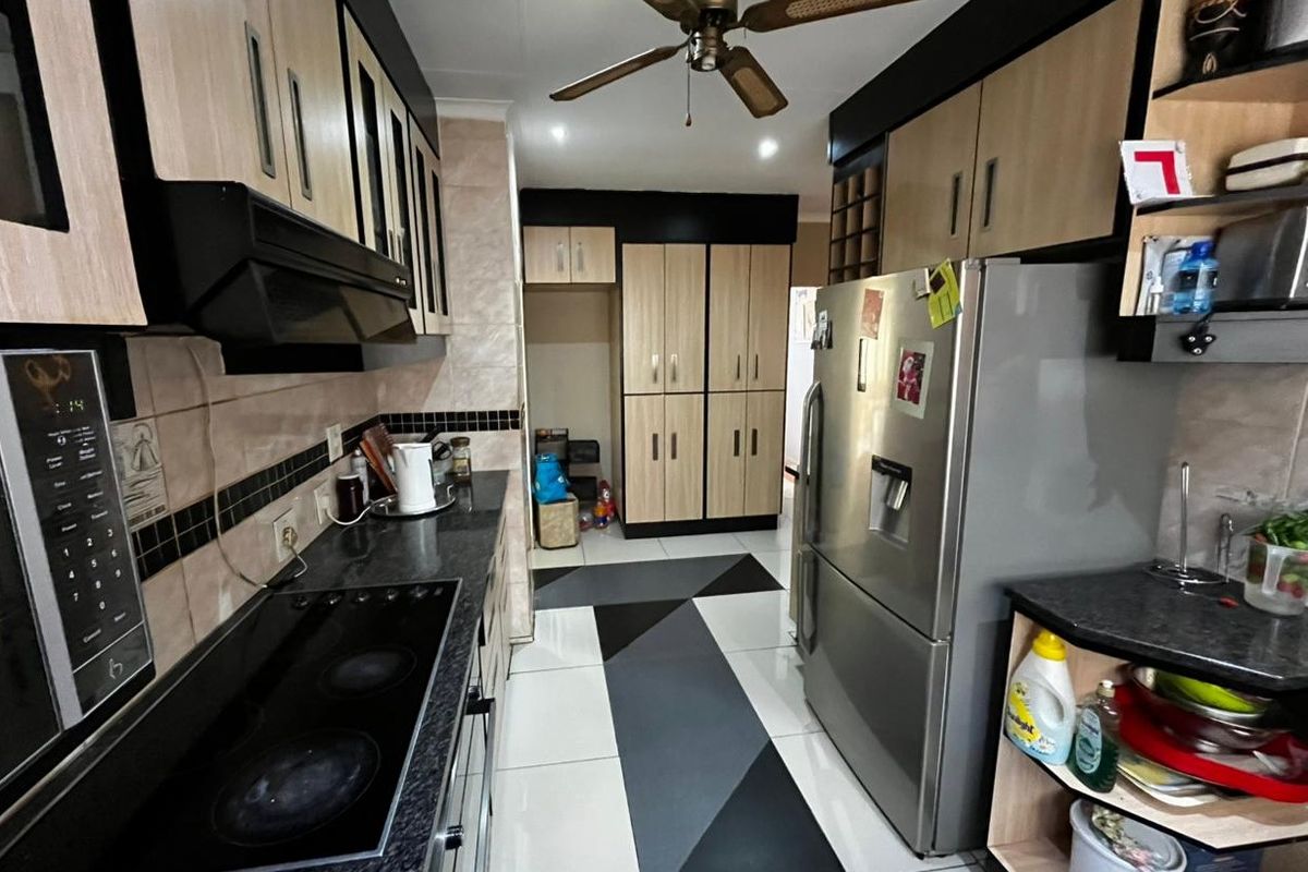 A functional kitchen featuring built-in cabinetry, a dark stone-look countertop, integrated hob, extractor fan, and tiled flooring with a geometric pattern.