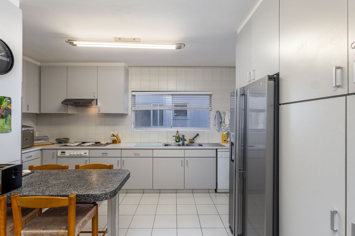 A functional kitchen featuring light grey cabinetry, tiled splashbacks, tiled flooring, and a built-in hob with extractor fan.