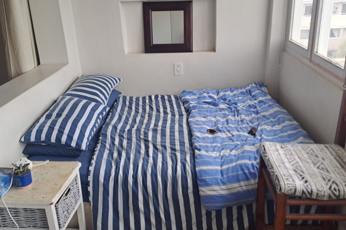 A compact bedroom featuring laminate flooring, a recessed wall niche, and large windows providing natural light.