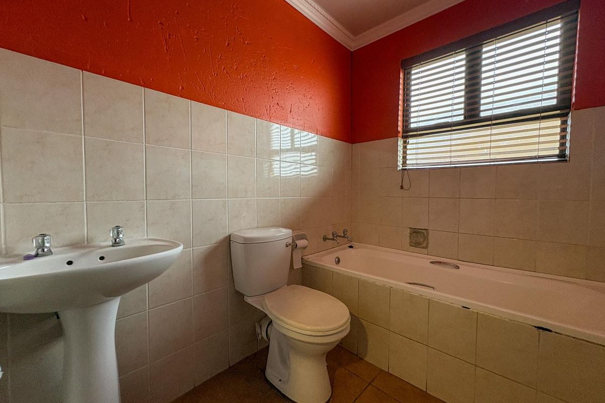 A functional bathroom featuring a pedestal basin, standard toilet, and a built-in bathtub with tiled splashbacks and a window with blinds.