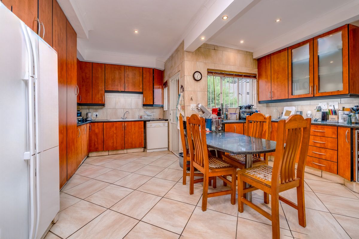 A functional kitchen featuring wood-toned cabinetry, granite countertops, tiled flooring, and an integrated dining area with recessed ceiling lighting.