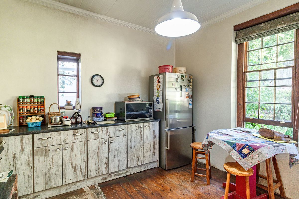 A functional kitchen featuring timber flooring, laminate cabinetry with a distressed finish, and natural light from timber-framed windows.