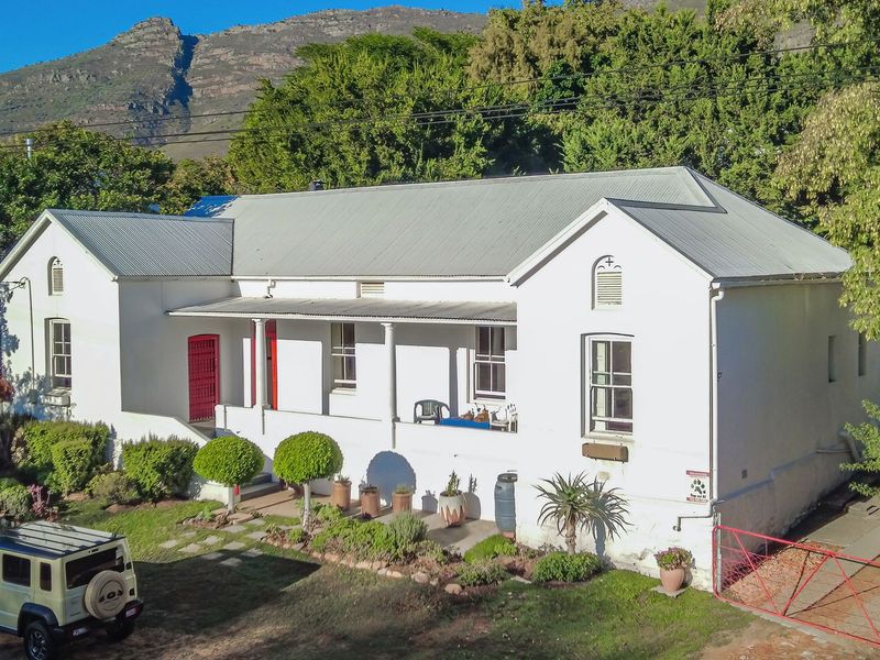 A charming single-story residence featuring a classic corrugated metal roof, a covered front veranda, and established garden surroundings against a mountain backdrop.
